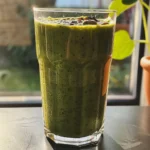 Close-up of a vibrant green smoothie topped with chia seeds, surrounded by fresh mango and strawberries.